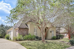 A two-story house with a brick facade, a front lawn, and a tree in front.