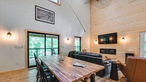 Un interior moderno con una mesa de comedor de madera, un sofá de cuero negro y un televisor montado en la pared.