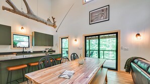 Una cocina moderna con una mesa de madera, taburetes de bar y un banco. Hay dos ventanas con vistas a árboles.