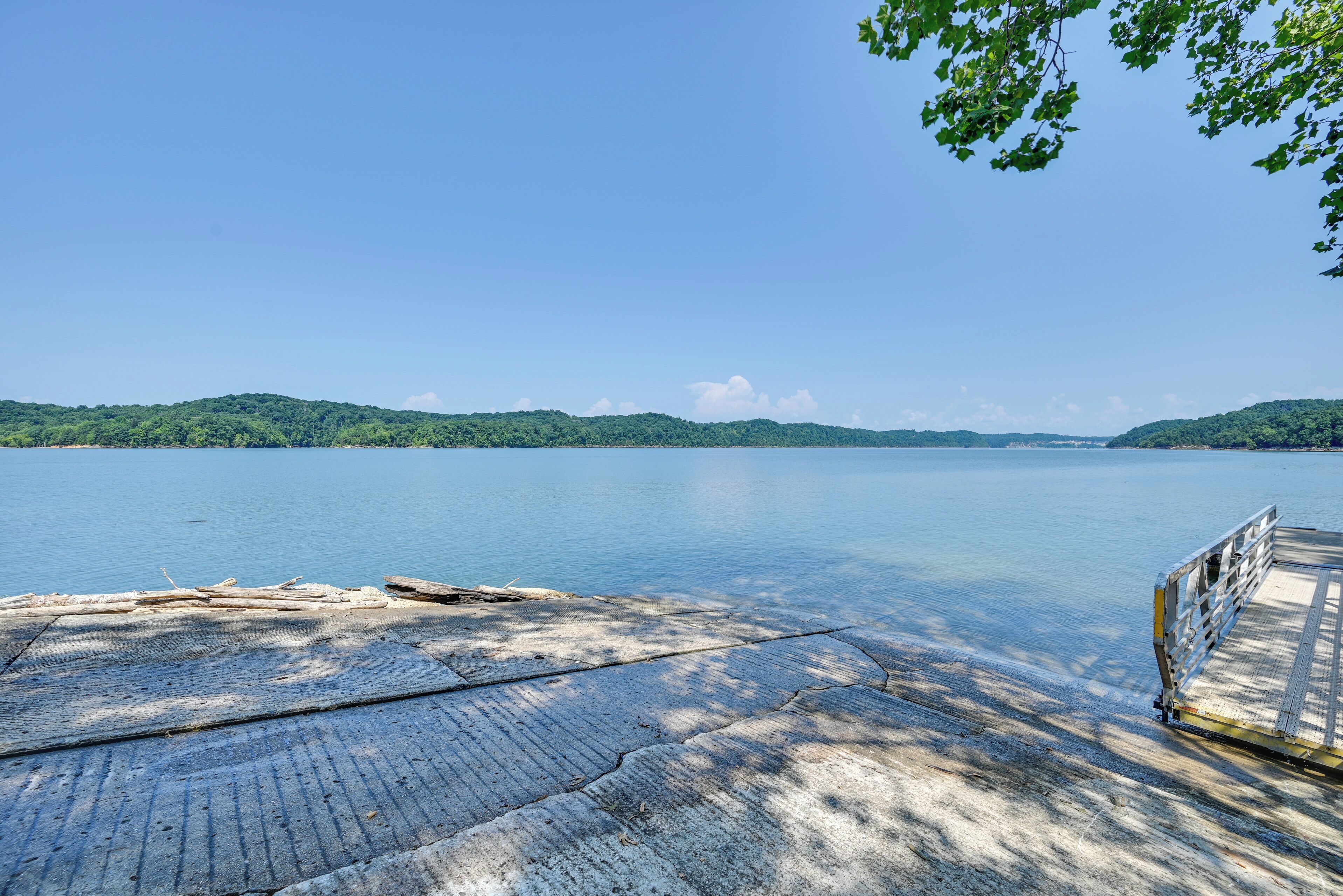 A concrete dock extending into a calm lake with a forested hill in the background.