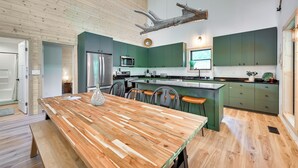 Una cocina moderna con una mesa de madera, armarios verdes y una viga de madera colgante.