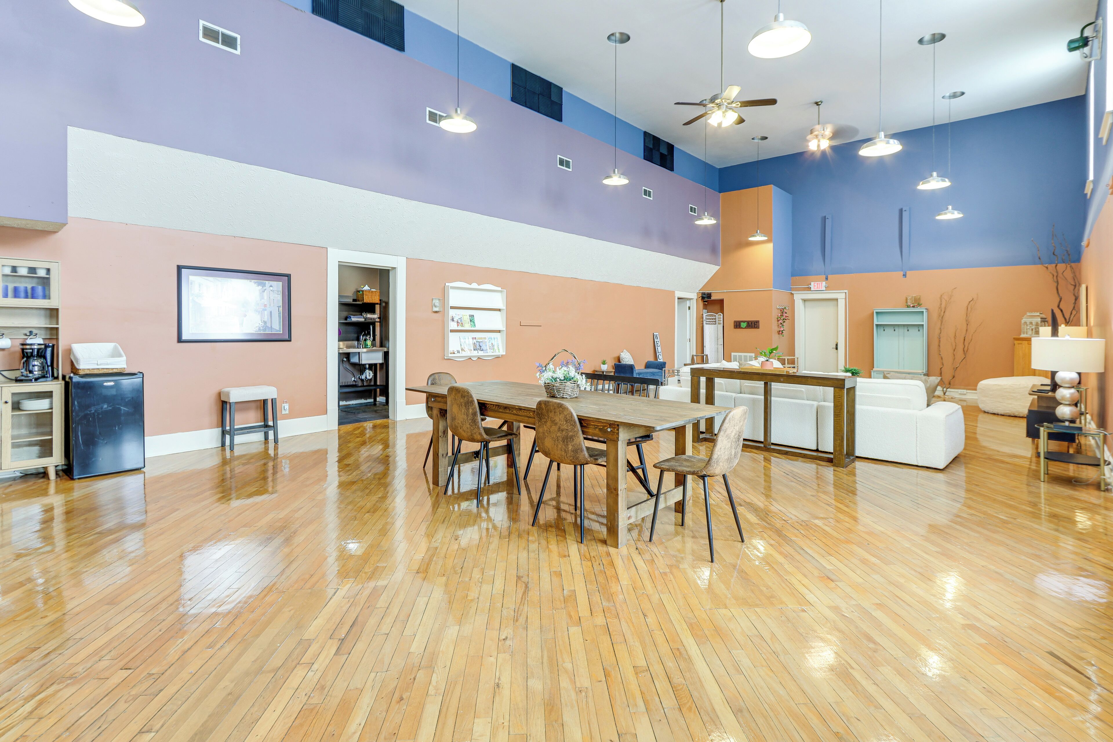 A spacious room with a wooden floor, a dining table with chairs, a kitchenette, and a seating area with a sofa and chairs.