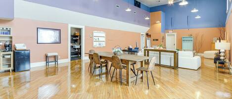 A spacious room with a wooden floor, a dining table with chairs, a kitchenette, and a seating area with a sofa and chairs.