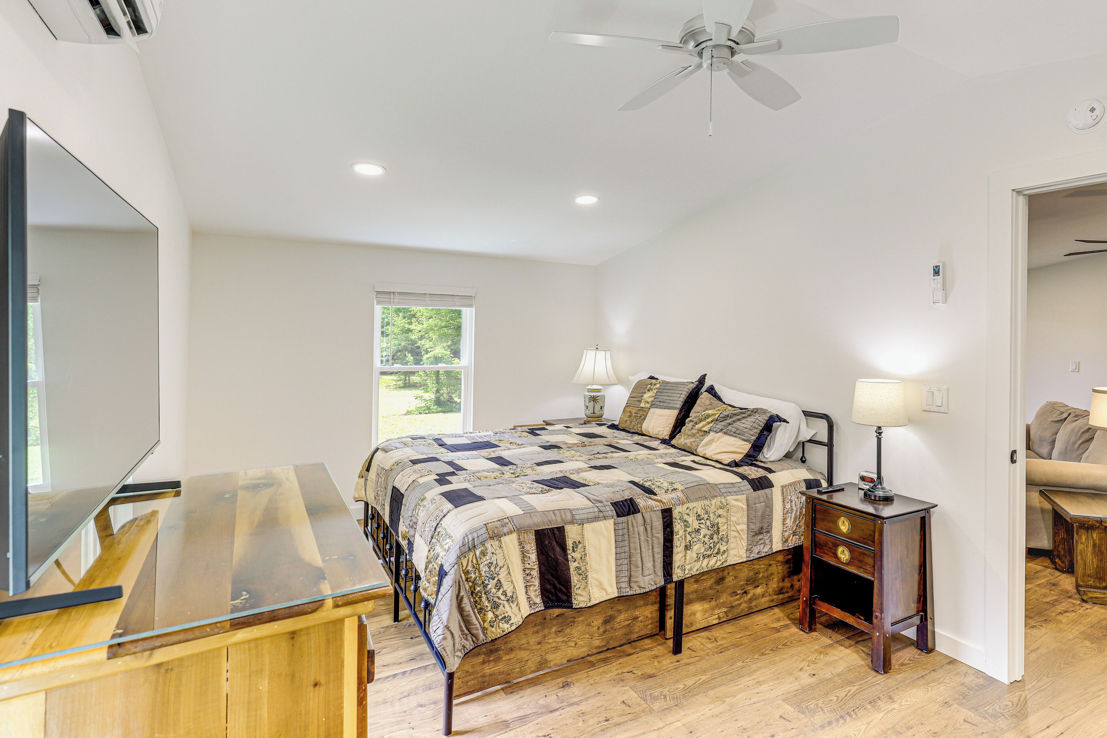 A bedroom with a wooden bed, a nightstand with a lamp, a ceiling fan, and a large mirror.