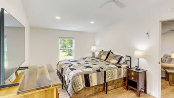 A bedroom with a wooden bed, a nightstand with a lamp, a ceiling fan, and a large mirror.