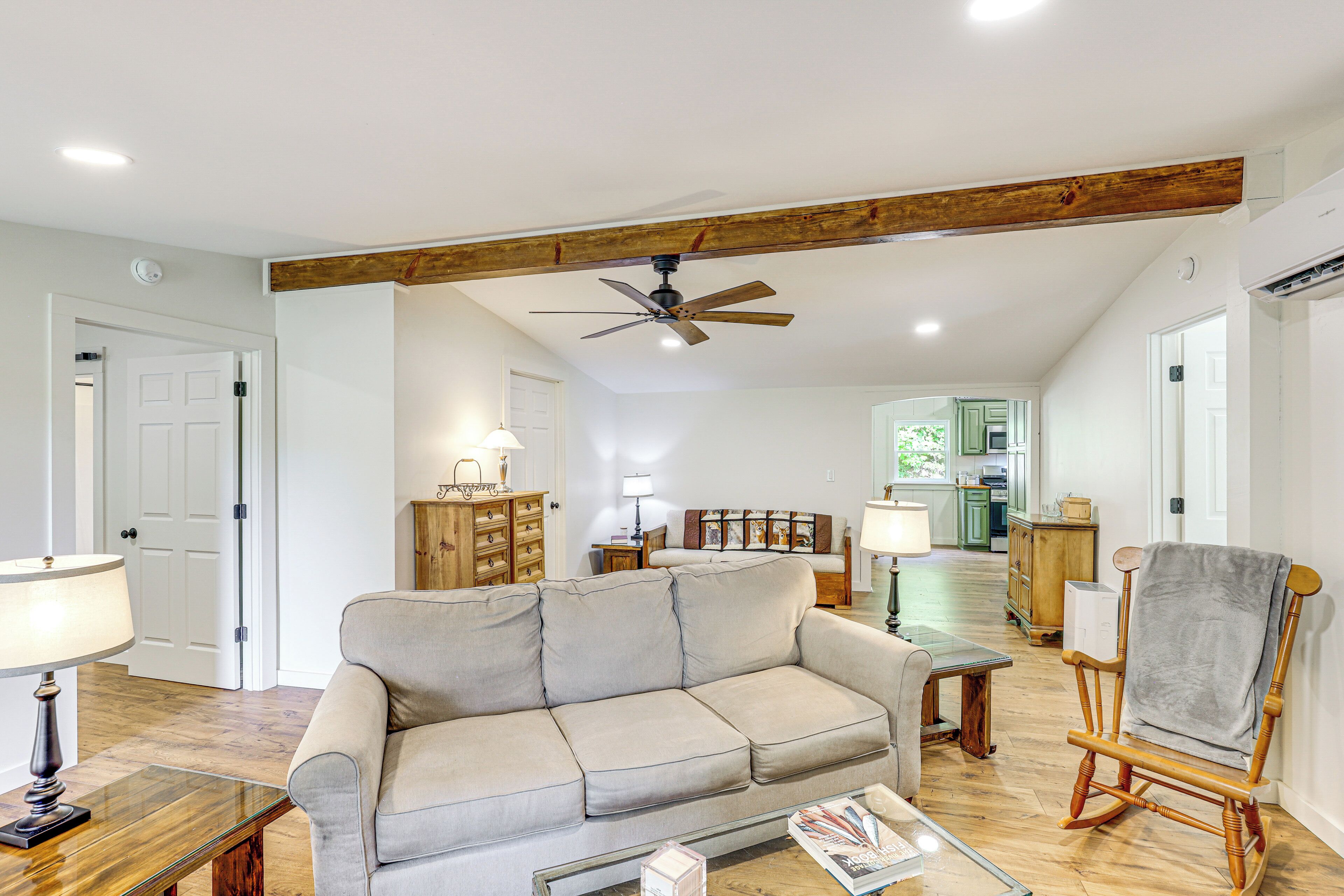 A living room with a sofa, a wooden rocking chair, a ceiling fan, and a kitchen in the background.