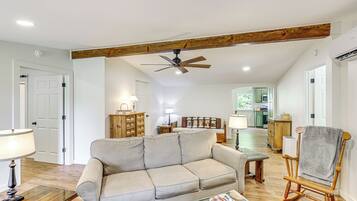 A living room with a sofa, a wooden rocking chair, a ceiling fan, and a kitchen in the background.