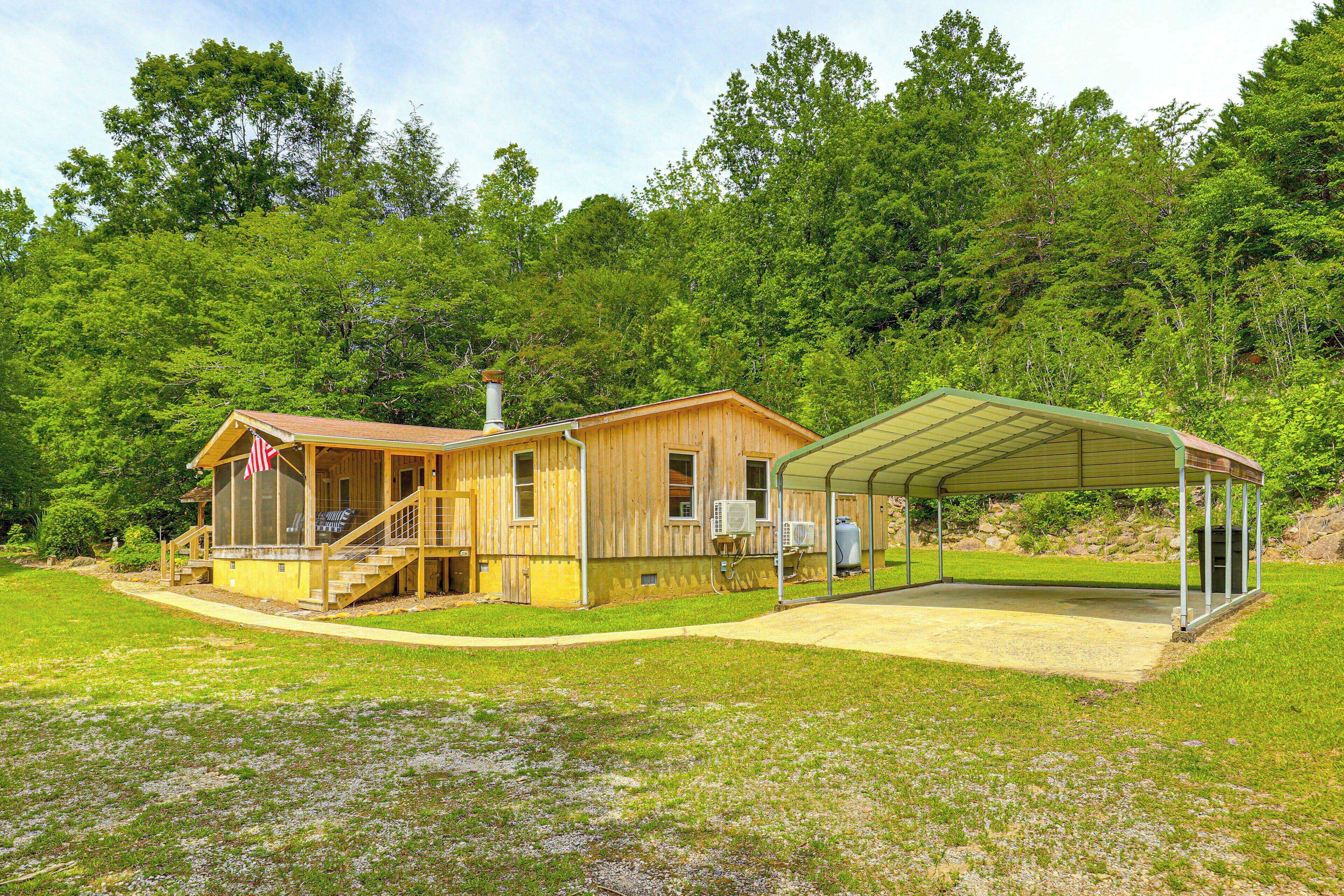 A wooden cabin with a covered porch and a small deck, surrounded by lush greenery.