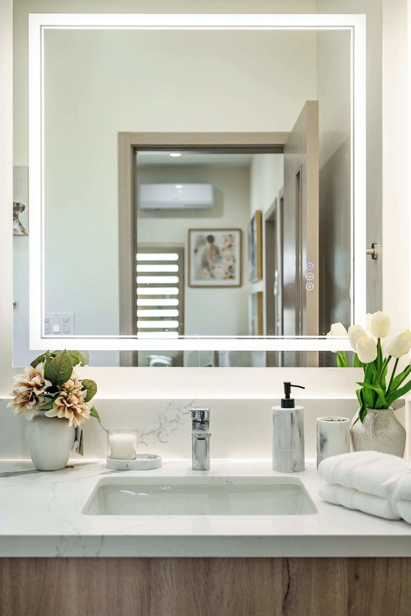 A bathroom with a large mirror, a sink, a toilet, and a shower area.