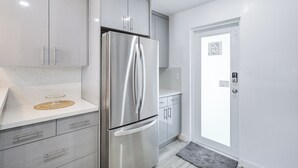 Una cocina moderna con un refrigerador de acero inoxidable, gabinetes grises y una encimera blanca.