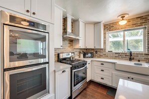 A modern kitchen with stainless steel appliances, white cabinetry, and a brick accent wall.