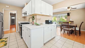 A modern kitchen with white cabinets, a central island, and a dining area with wooden chairs. - Cozy Modern 4B Family Retreat House (Ontario)