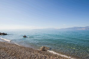 A pebbly beach with clear water and distant mountains. - Seaside Retreat in Diminio (Sikyona)