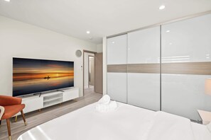 Moderni hotellihuone, jossa on suuri litteänäyttöinen televisio, valkoisilla lakanoiden peitetty sänky, puulattia ja liukuovellinen vaatekaappi.