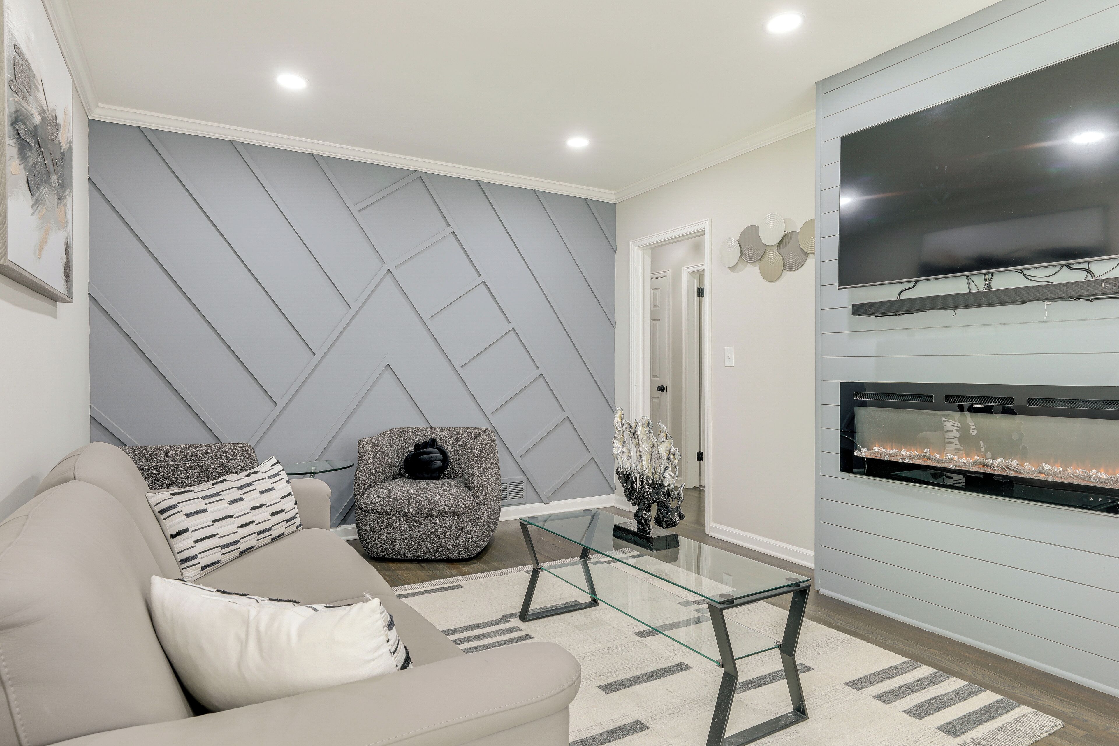A modern living room with a sofa, a glass coffee table, a fireplace, and a wall-mounted TV.