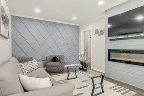 Ein modernes Wohnzimmer mit einer Couch, einem Glastisch, einem Kamin und einem an der Wand montierten Fernseher.