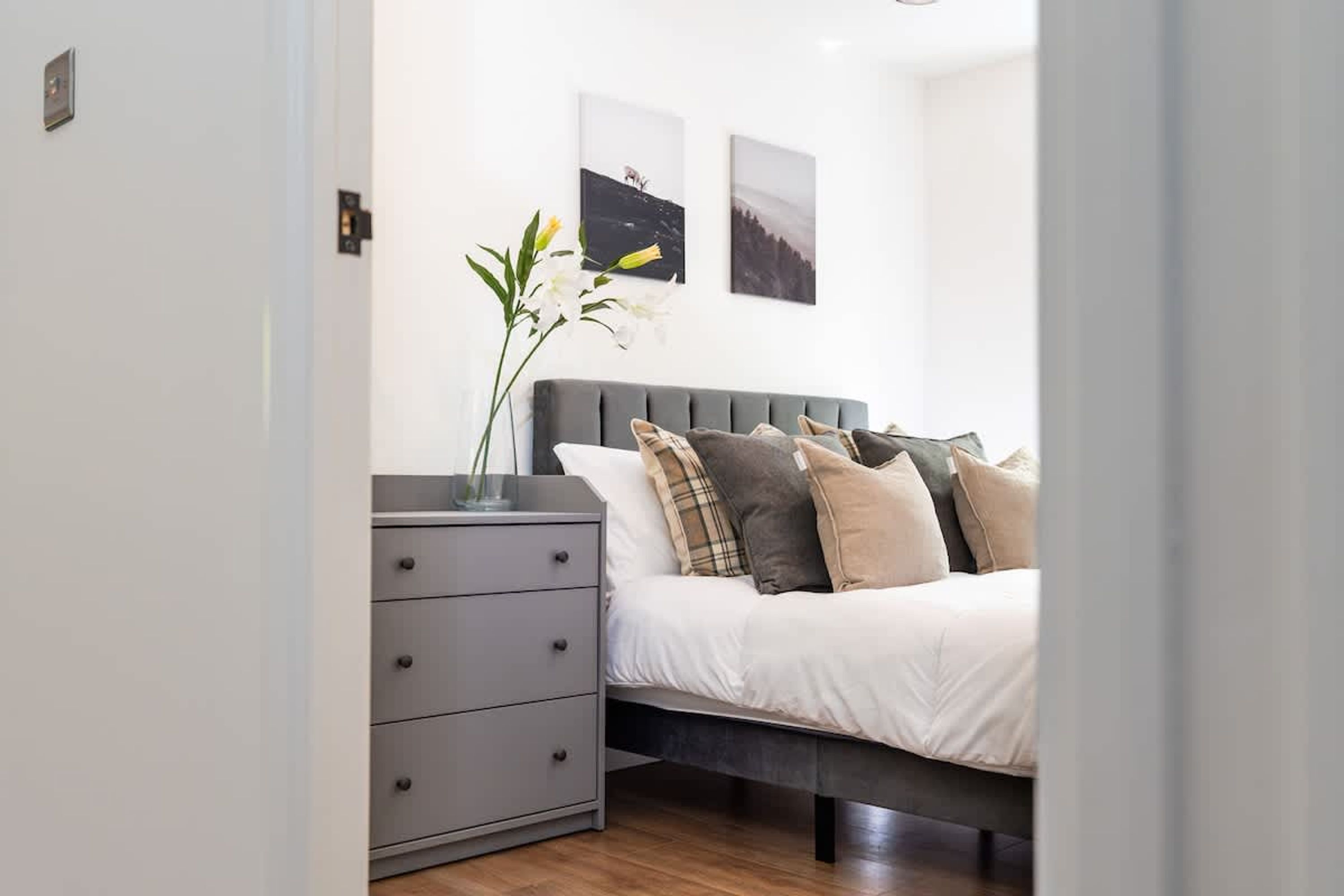 Een slaapkamer met een bed, nachtkastje, kaptafel en twee aan de muur bevestigde foto's.