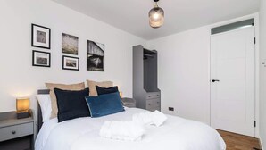 Un lit bien fait, avec du linge de lit blanc, une table de chevet avec une lampe et une armoire.