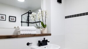 Une salle de bain avec un lavabo blanc, un miroir, un porte-serviettes et une orchidée en pot.