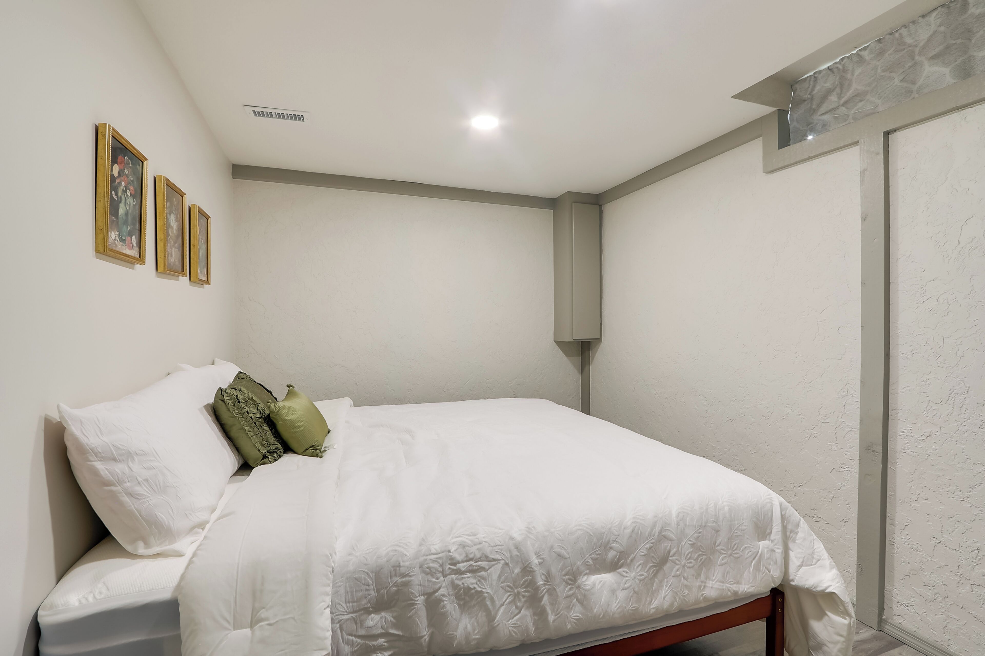 Una cama bien hecha con ropa blanca y almohadas verdes, un aplique de pared y cuadros en la pared.