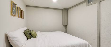 Una cama bien hecha con ropa blanca y almohadas verdes, un aplique de pared y cuadros en la pared.