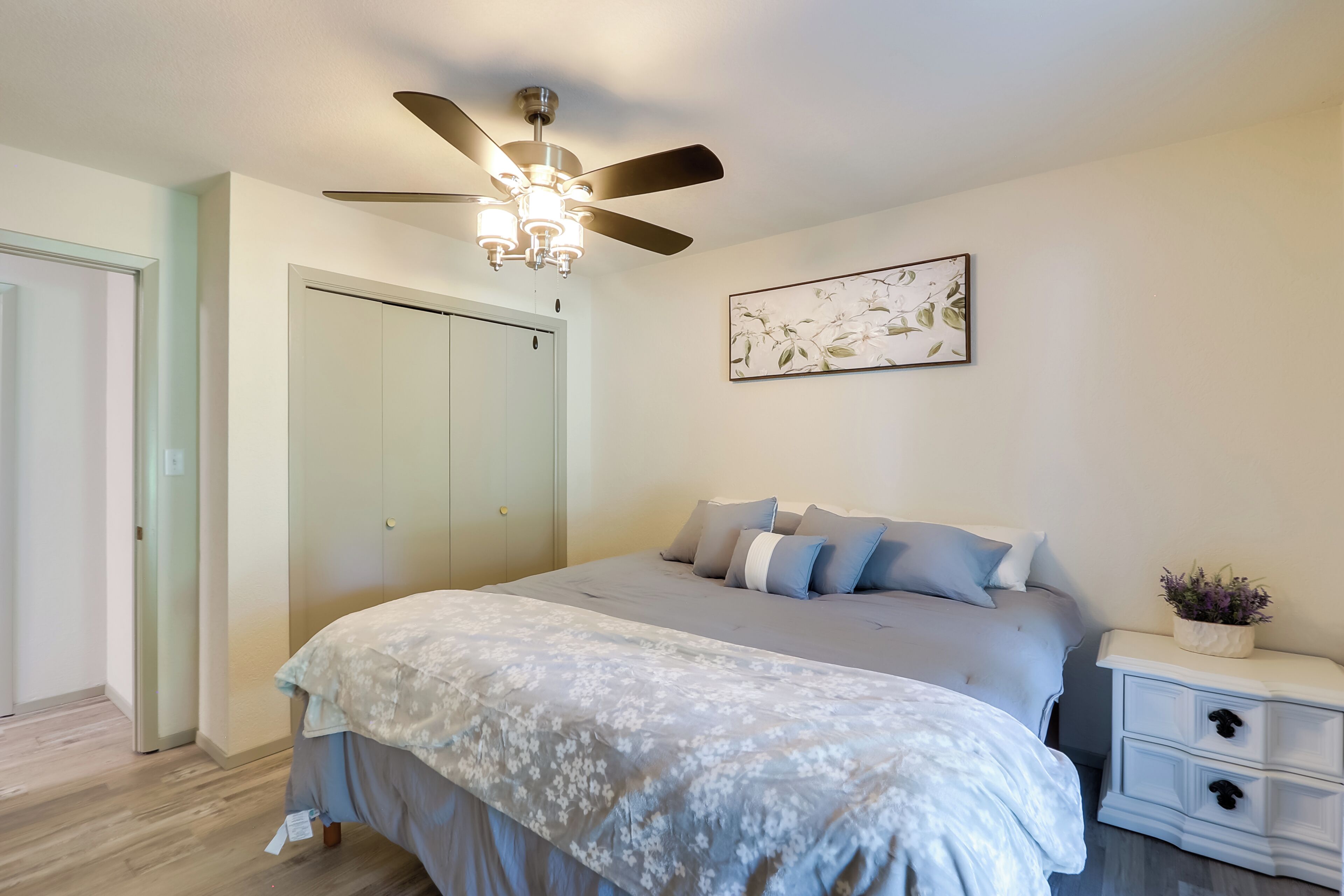 Une chambre à coucher comprenant un lit, un ventilateur de plafond, une table de chevet, une œuvre d’art accrochée au mur et une armoire.
