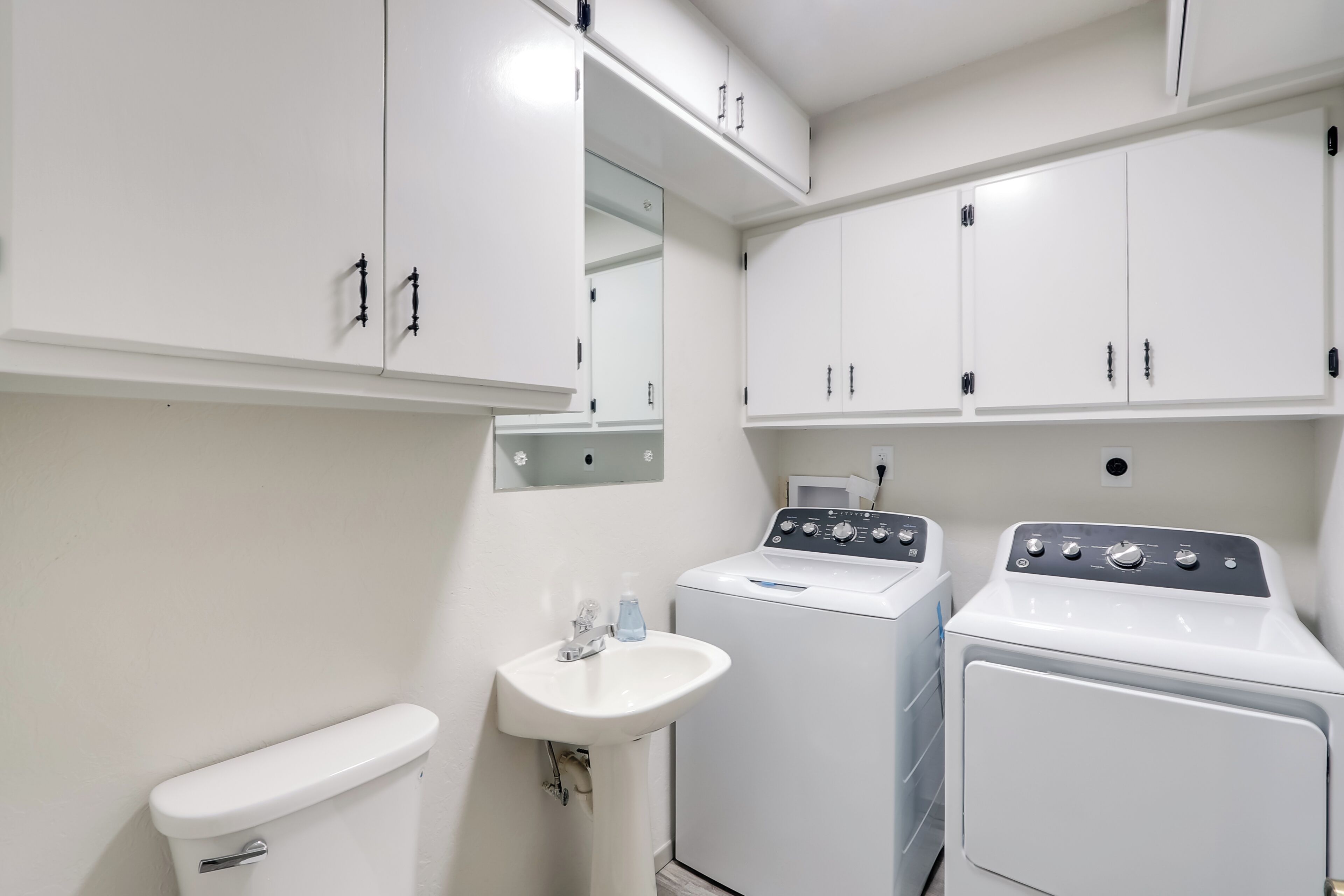 Une petite salle de bain comprenant des toilettes, un lavabo et deux machines à laver superposées.