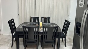 Zona pranzo con tavolo apparecchiato per quattro, circondato da sedie, un frigorifero e un cartello che indica il divieto di fumare al chiuso.