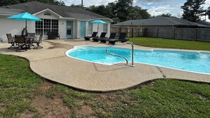 Un giardino sul retro con piscina, sedie a sdraio e tavolo da esterno.