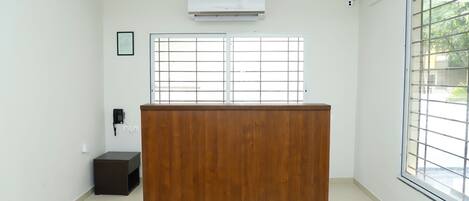 Una habitación con mostrador de recepción de madera, ventilador de techo, equipo de aire acondicionado, teléfono y ventana con vistas a zonas verdes.
