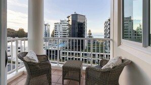 Un balcon doté de meubles en osier, offrant une vue sur des bâtiments modernes et une étendue d’eau.