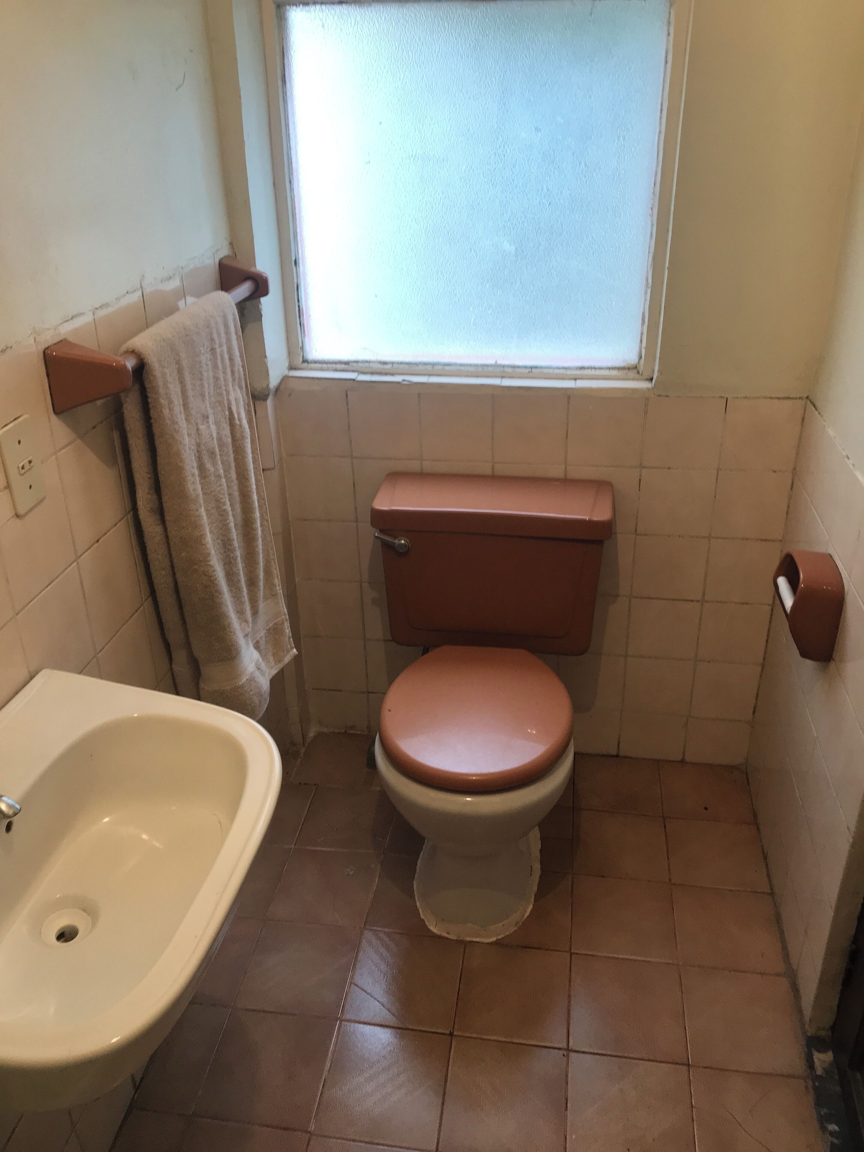 A small bathroom with a toilet, a sink, and a window.