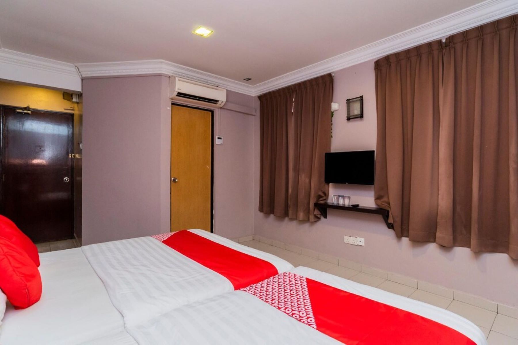 Quarto de hotel com duas camas, uma televisão presa na parede e cortinas castanhas.