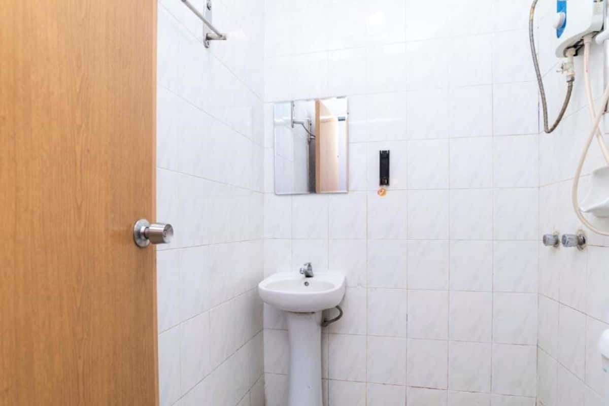 Ein kleines, sauberes Badezimmer mit wei ßen Fliesen, einem Standwaschbecken, einem Spiegel und einem Duschkopf.