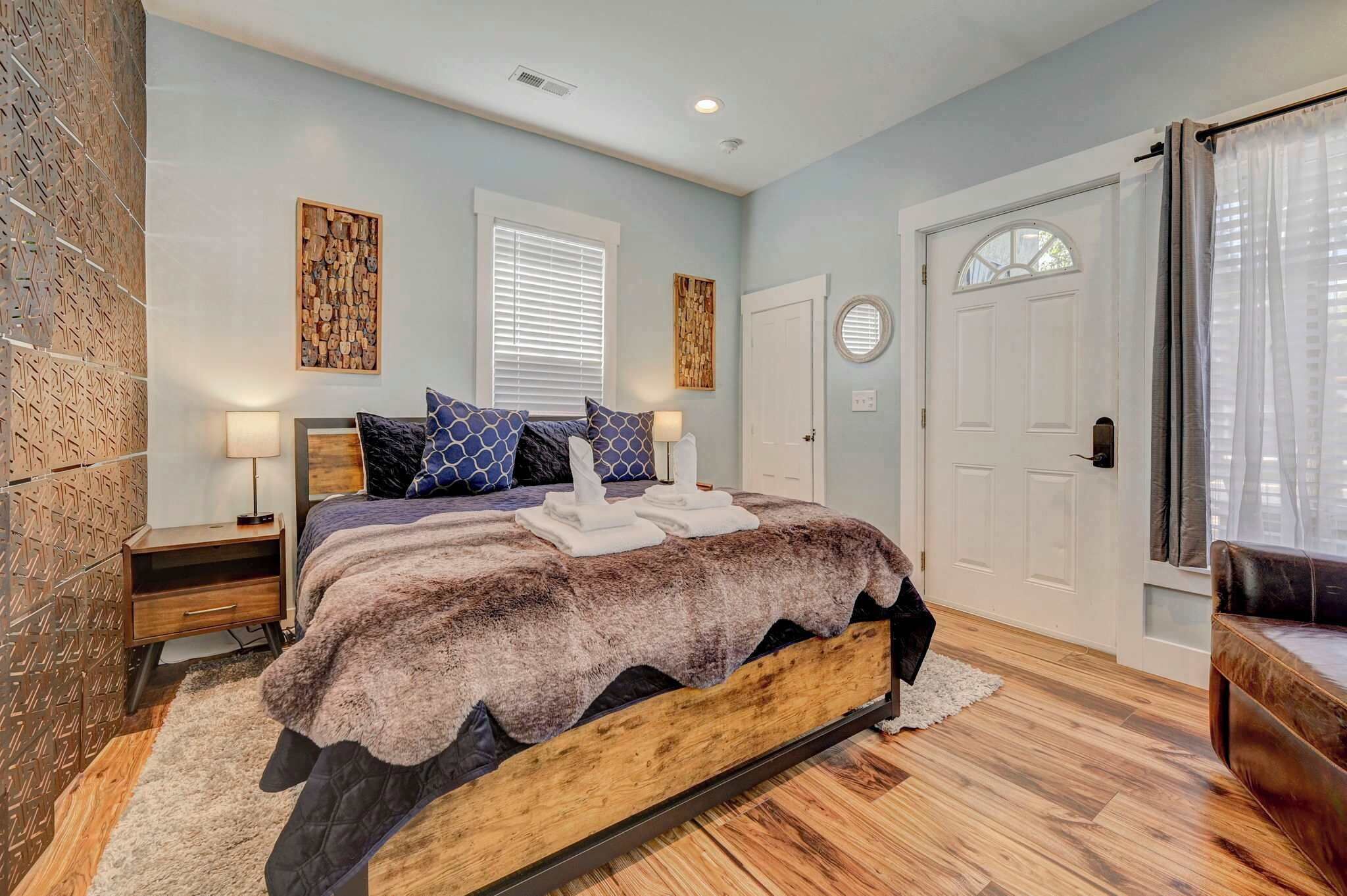 Een slaapkamer met een houten bed, een nachtkastje, een wandklok en een deur met een raam.