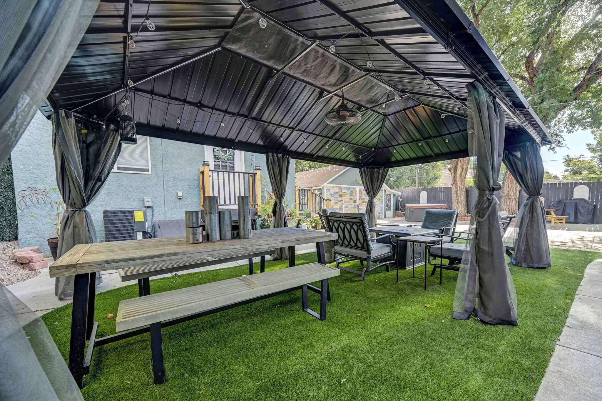 Une terrasse extérieure couverte, avec une table et des bancs en bois, entourée d’une pelouse.