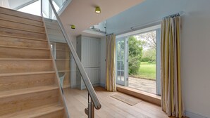 A staircase with wooden steps and a metal handrail leading to a room with a large sliding glass door to a garden. - Drift Cottage, Salthouse, Norfolk (Salthouse)