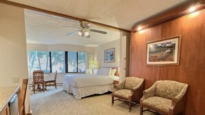 Ein Hotelzimmer mit einem Bett, zwei Sesseln, einem Schreibtisch und einem Deckenventilator.