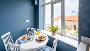 A dining area with a table set for breakfast, a window with a view of the outside, and a potted plant on the windowsill. - The Look Out, Sheringham, Norfolk (Sheringham)