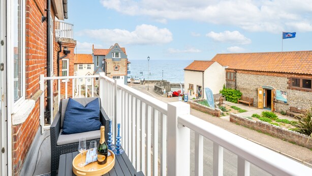 A balcony with a sofa, a tray with glasses and a bottle, and a view of the sea and buildings. - The Look Out, Sheringham, Norfolk (Sheringham)