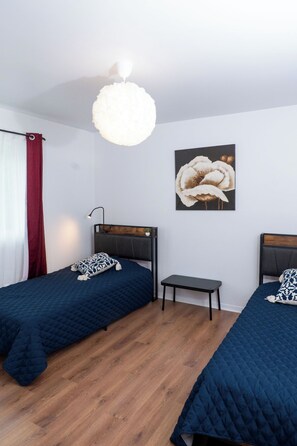 A bedroom with two beds, a bedside table, a hanging light fixture, and a wall-mounted picture.