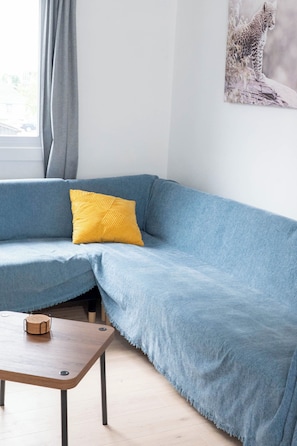 Un canapé d’angle avec un coussin jaune, une table basse en bois et un tableau accroché au mur.