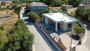A modern two-story house with a flat roof, a small patio with outdoor furniture, and a view of the sea. - Ninalma Villa (Rhodes)