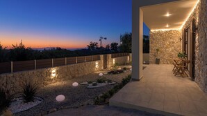 A modern house with a stone exterior, a patio with a table and chairs, and a view of the landscape. - Ninalma Villa (Rhodes)