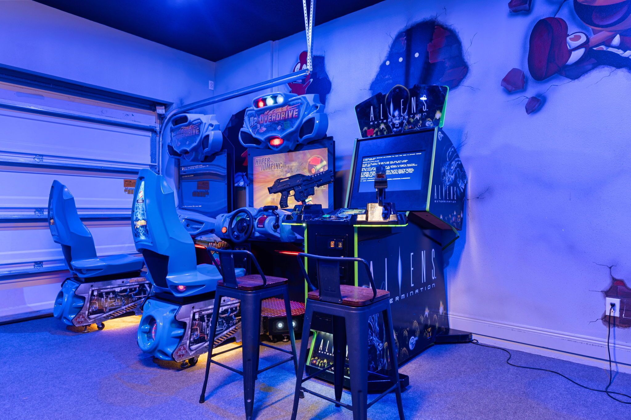 Un espace de jeu équipé de bornes d’arcade, de chaises et d’un écran affichant un jeu.