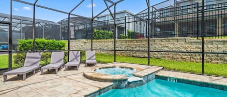 A swimming pool with lounge chairs and a hot tub, surrounded by a glass enclosure.