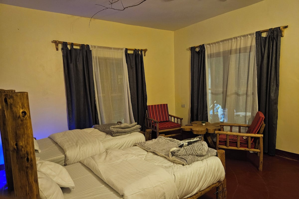 A room with a wooden bed, two chairs, a small table, and a TV.