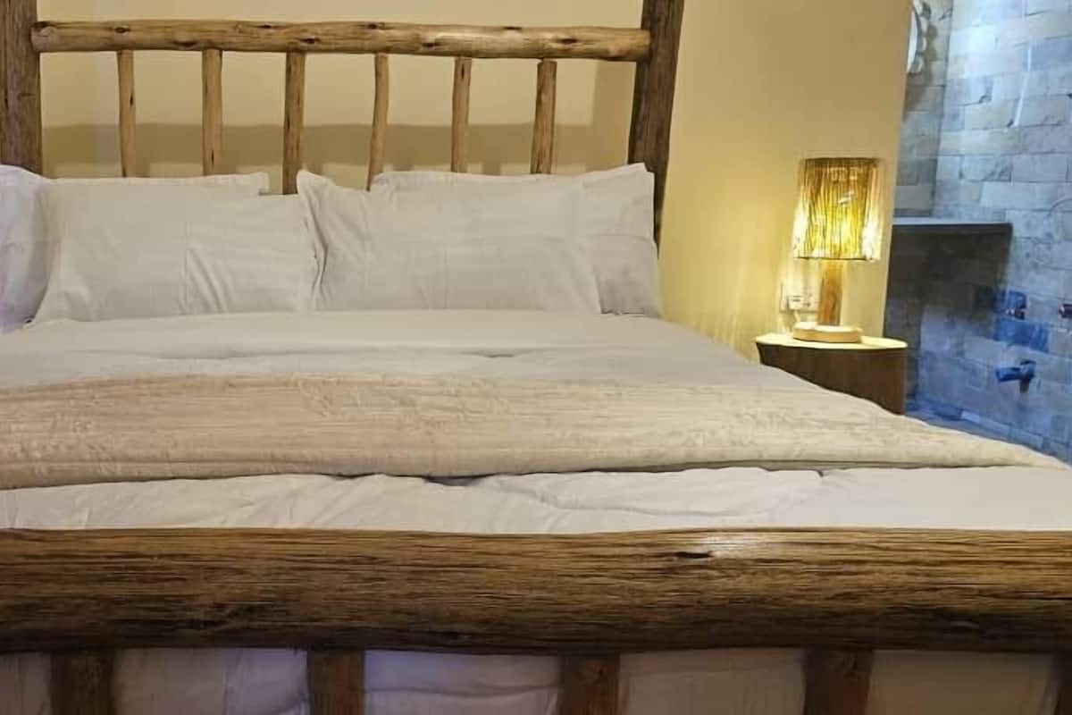 A bed with a wooden headboard, white bedding, and a nightstand with a lamp.