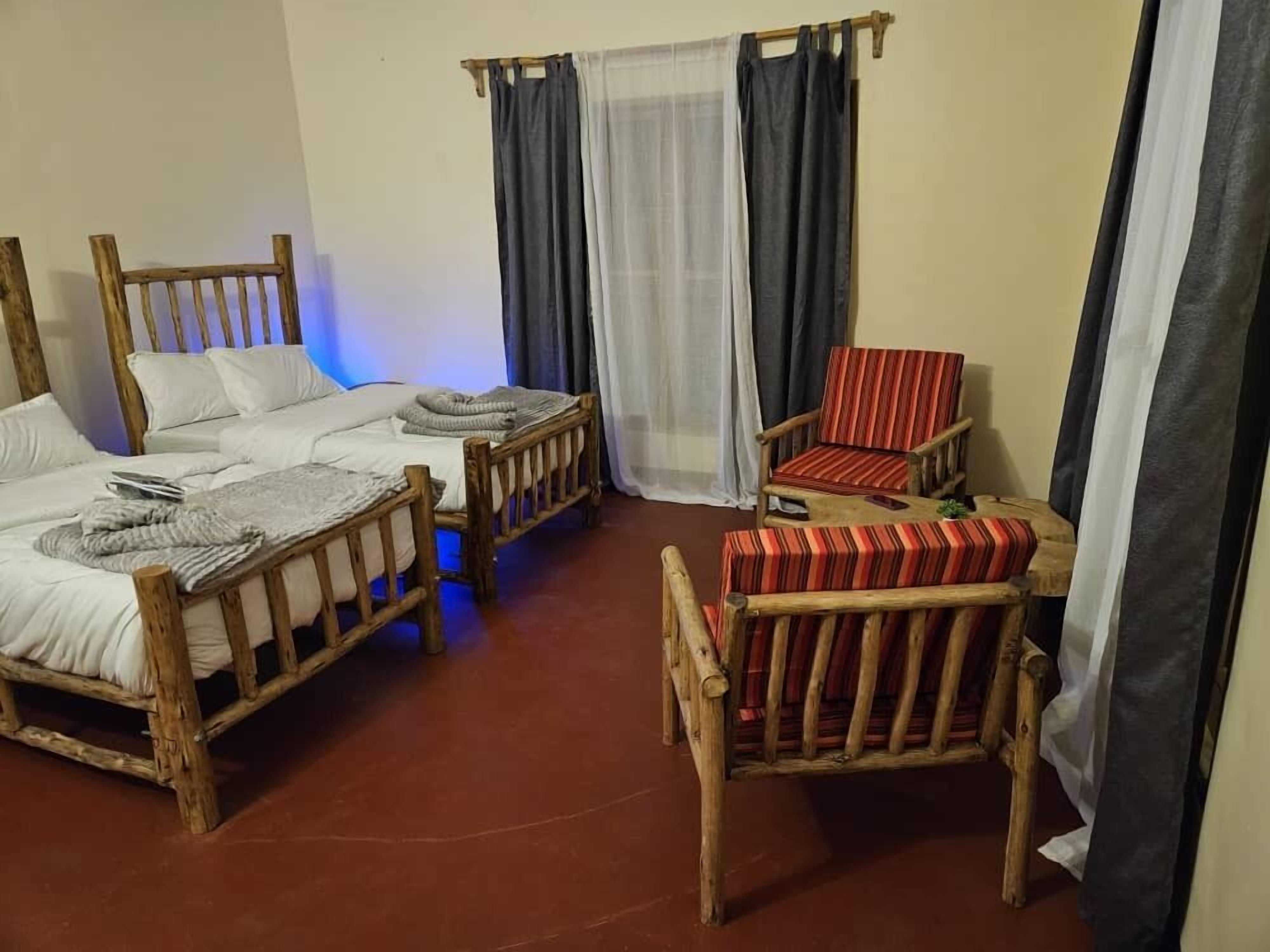 Una habitación con dos camas de madera, una silla a rayas rojas y una mesa de madera.