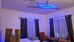 A room with two beds, wooden chairs, a small table, and a unique ceiling light fixture.